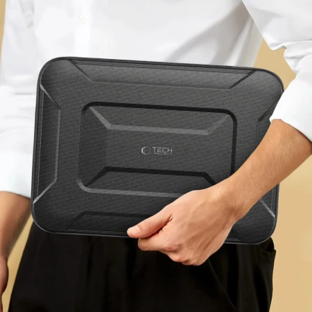 Osoba w bialej koszuli niesie zamkniete etui na laptopa trzymajac je z boku przy biodrze