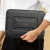 Osoba w bialej koszuli niesie zamkniete etui na laptopa trzymajac je z boku przy biodrze