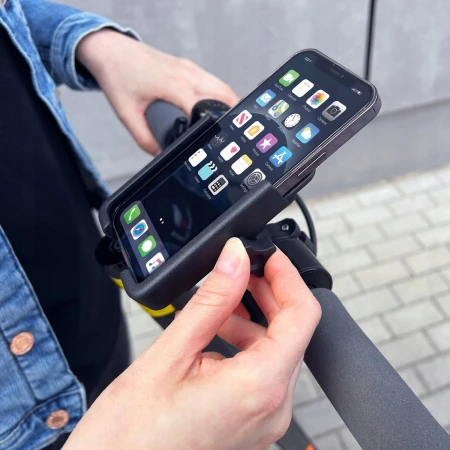 Wozinsky WBHBK3 w użyciu — dłonie wkładają smartfon do uchwytu na kierownicy hulajnogi