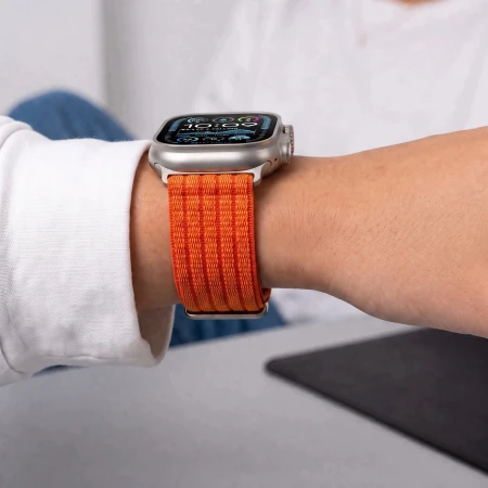 Apple Watch Ultra z pomarańczowym paskiem Nylon Sport na nadgarstku kobiety w białej koszuli