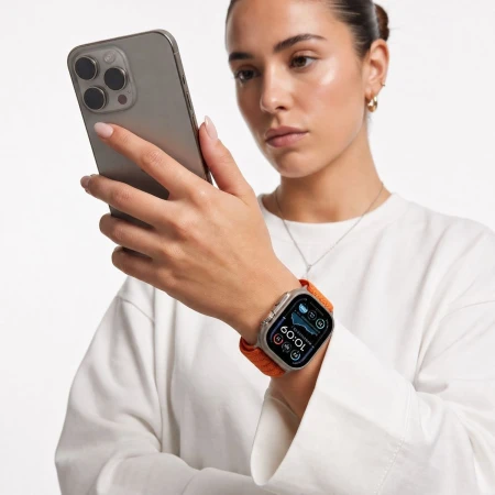 Kobieta trzyma telefon przy twarzy – Apple Watch z pomarańczowym paskiem Nylon Sport na nadgarstku