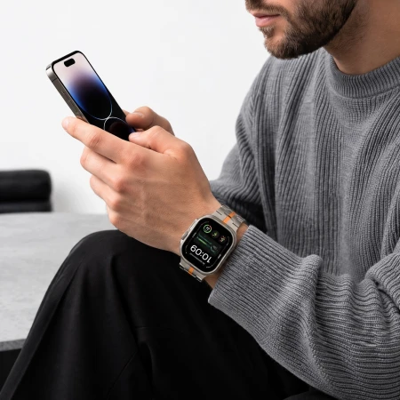 Mężczyzna w szarym swetrze z telefonem – Apple Watch Ultra z bransoletą Stainless Titanium/Orange