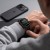 Dłoń dotyka ekranu Apple Watch z czarną bransoletą Stainless – telefon na stole