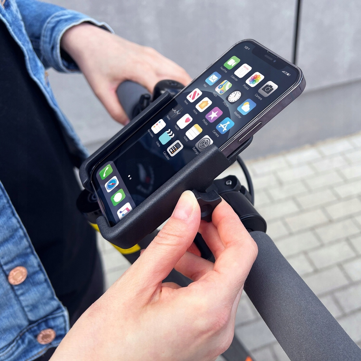 Wozinsky WBHBK3 w użyciu — dłonie wkładają smartfon do uchwytu na kierownicy hulajnogi