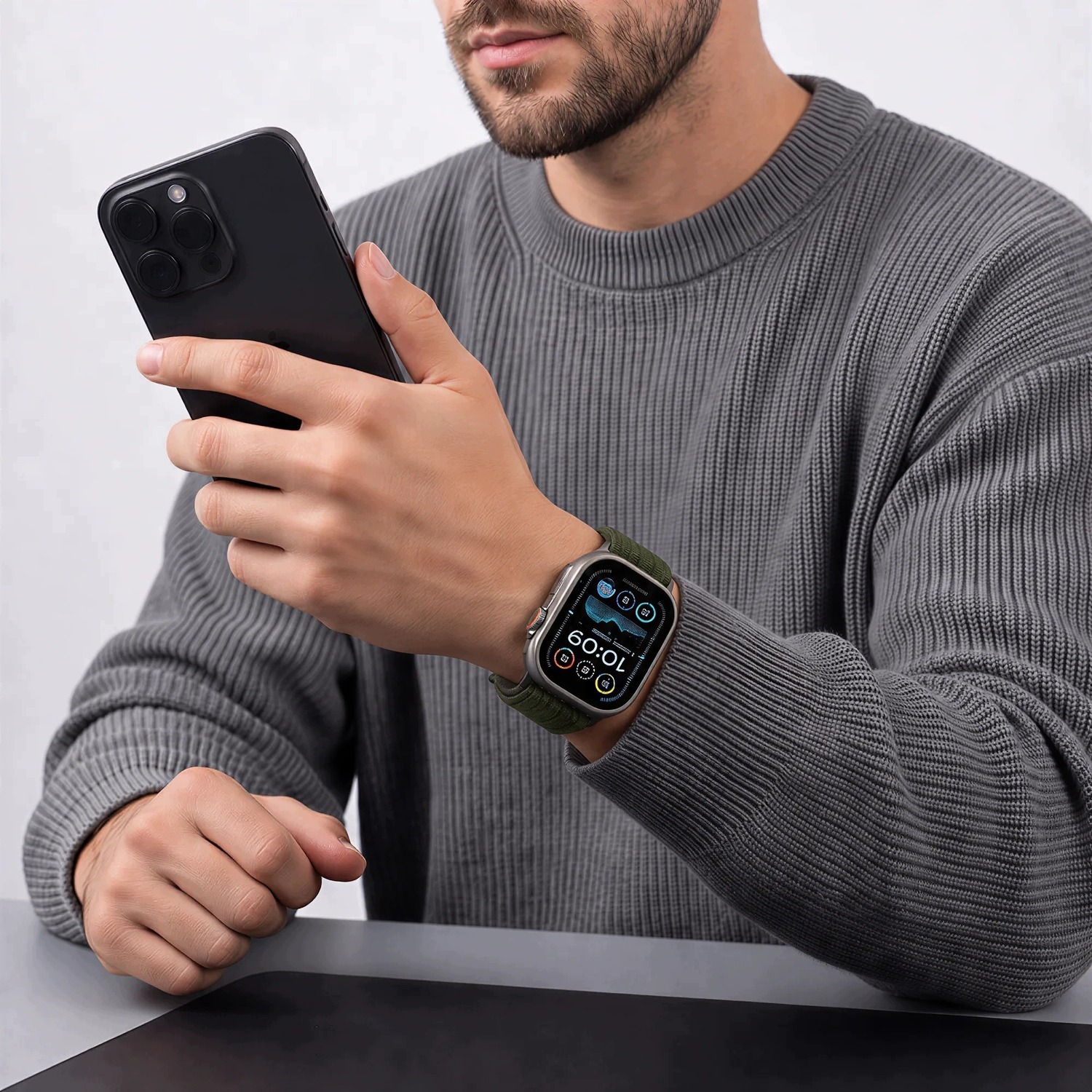 Mężczyzna w szarym swetrze z telefonem – Apple Watch z zielonym paskiem Nylon Sport na nadgarstku